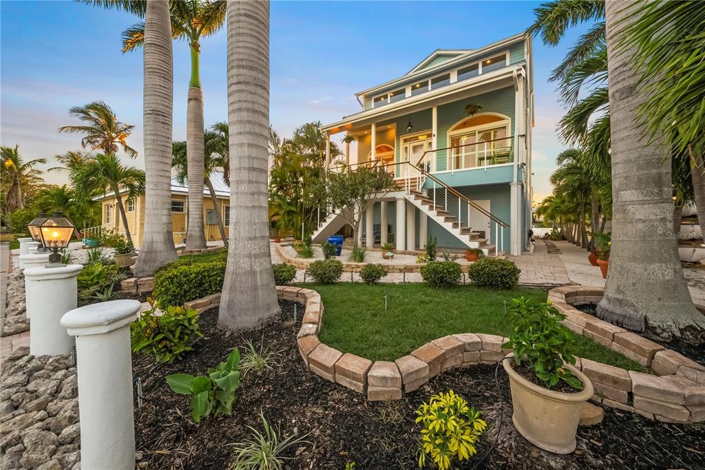 A light blue elevated house with a front staircase and palm trees in the yard — 791 BROADWAY STREET, LONGBOAT KEY, FL