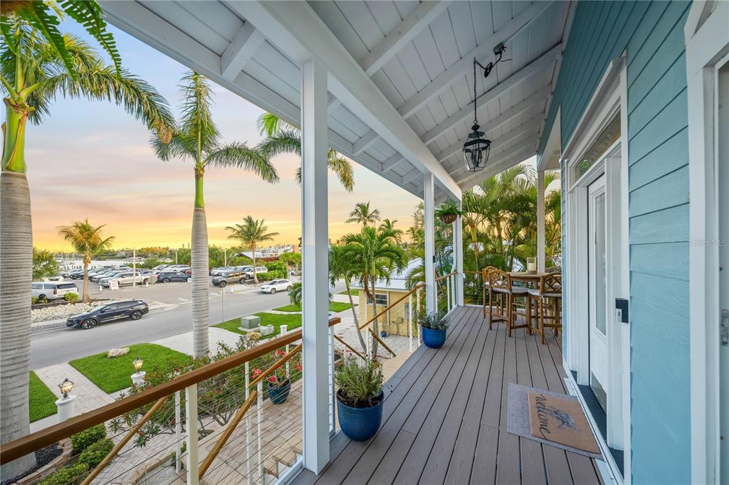 A covered wooden balcony overlooks a street with palm trees and parked cars at sunset — 791 BROADWAY STREET, LONGBOAT KEY, FL