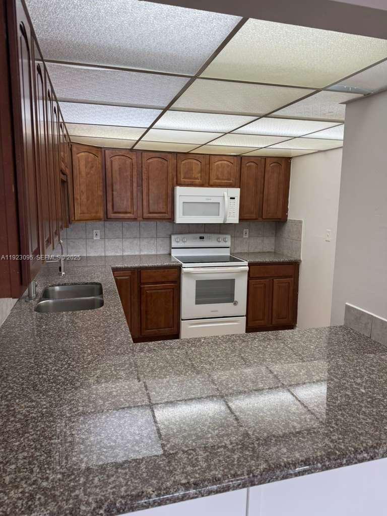 A kitchen features dark wood cabinets, granite countertops, white appliances, and a drop ceiling — 7000 NW 186th St # 226, Hialeah FL 33015, HIALEAH, FL