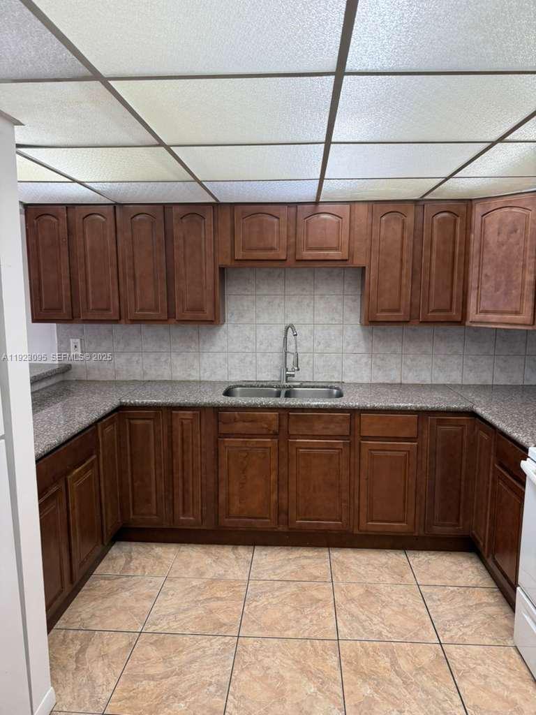A kitchen features dark wood cabinets, granite countertops, a double sink, and tiled flooring — 7000 NW 186th St # 226, Hialeah FL 33015, HIALEAH, FL