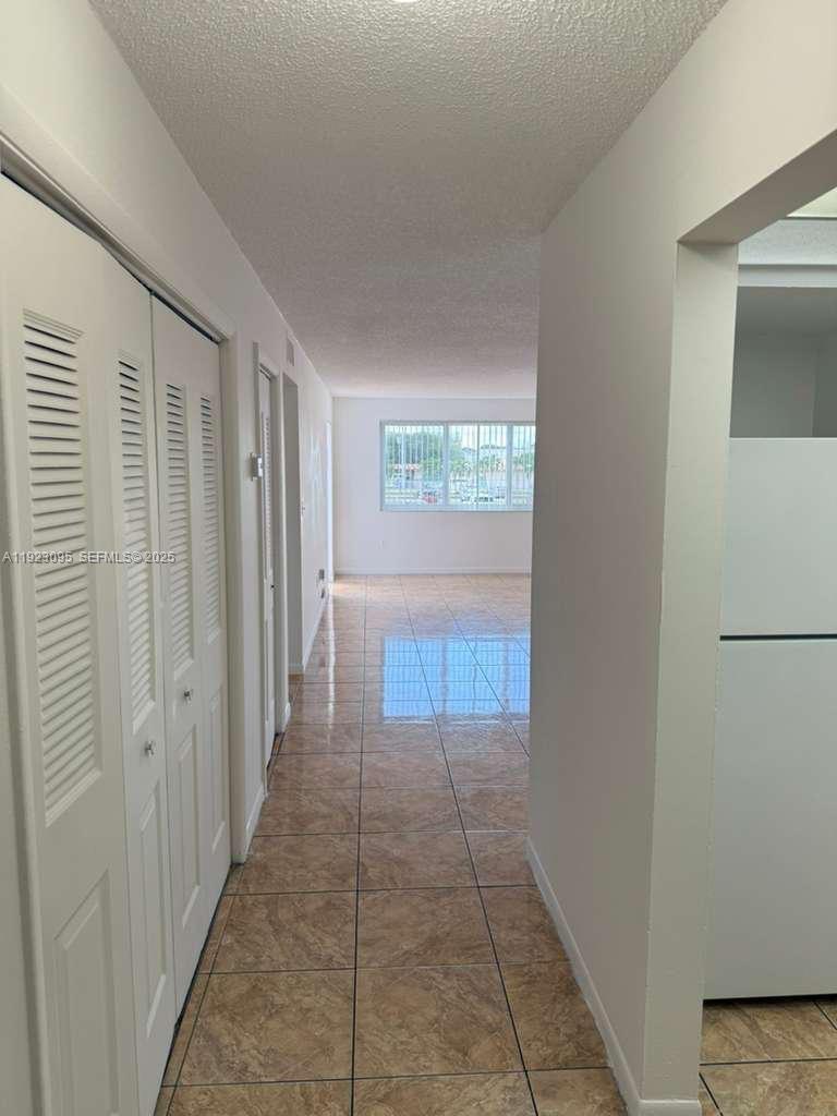 A hallway with tiled floors leads to a living area with a large window — 7000 NW 186th St # 226, Hialeah FL 33015, HIALEAH, FL