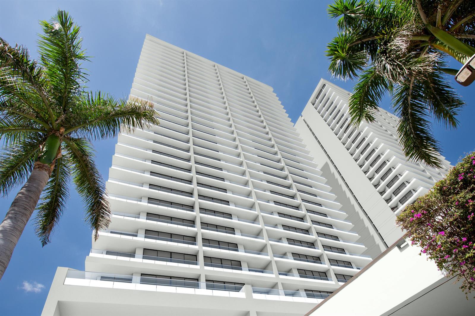 A low-angle view of a tall white residential building with balconies framed by palm trees — 525 S Flagler Drive, West Palm Beach FL 33401, WEST PALM BEACH, FL