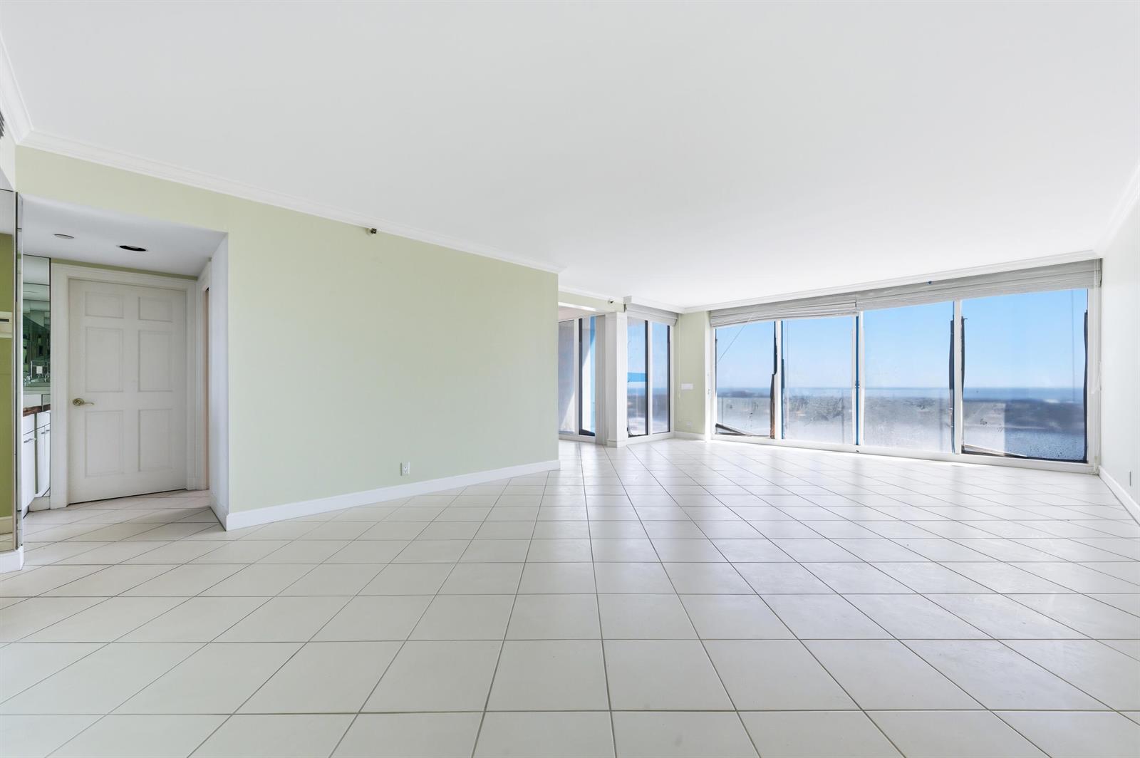 An empty room with light green walls, white tile flooring, and large windows overlooking water — 525 S Flagler Drive, West Palm Beach FL 33401, WEST PALM BEACH, FL