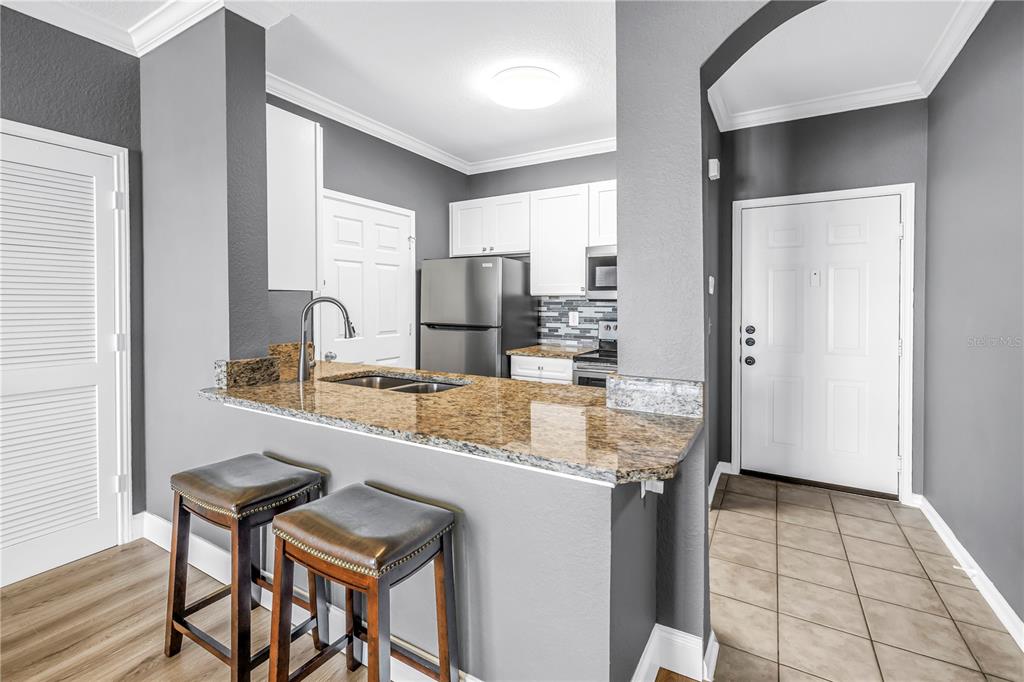 A kitchen with granite countertops, stainless steel appliances, and a breakfast bar with two stools — 1216 S MISSOURI AVENUE UNIT 415, CLEARWATER, FL