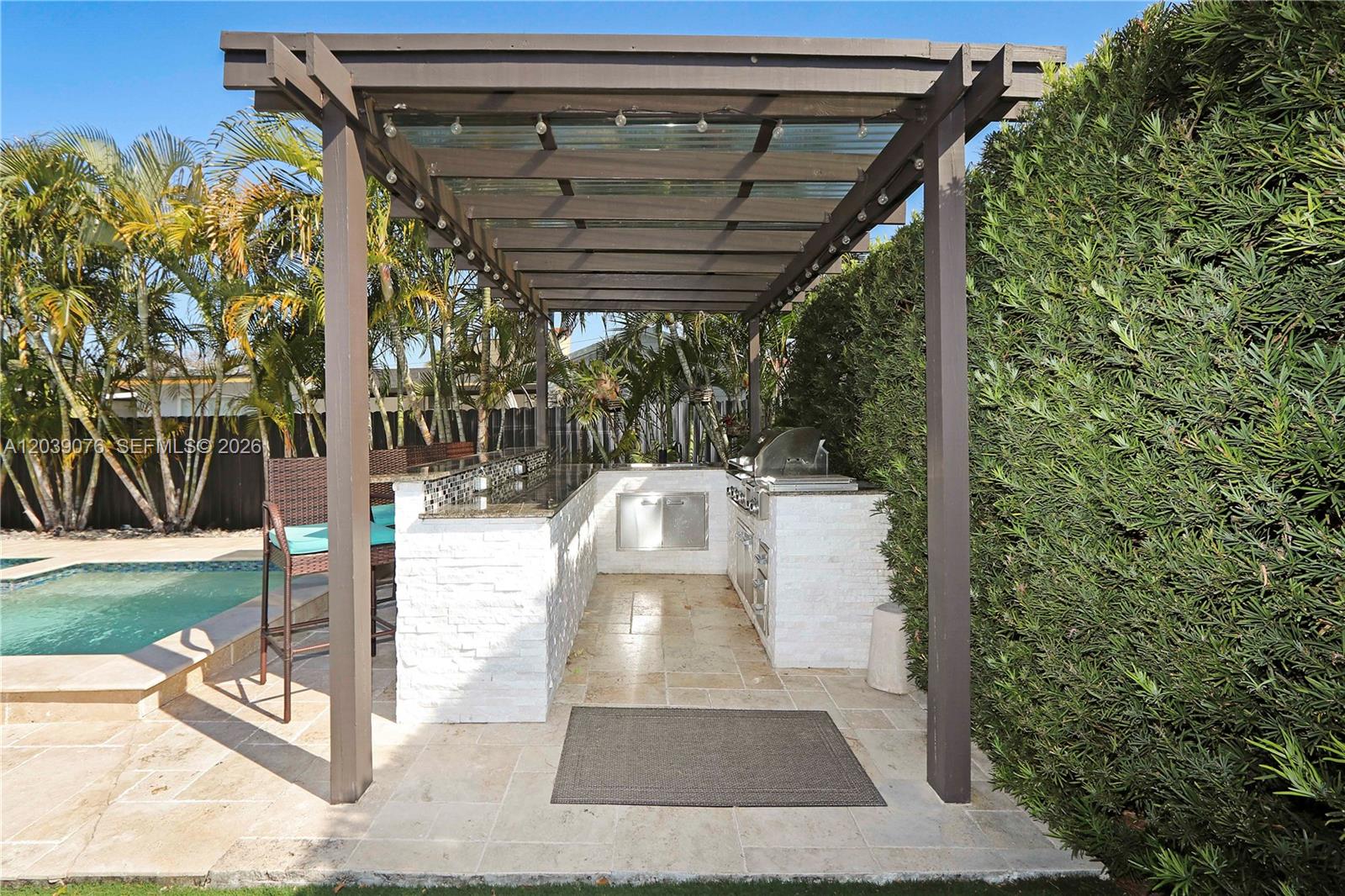 An outdoor kitchen with a pergola, stone counters, and a grill sits beside a pool — 6751 SW 13th St, Miami FL 33144, MIAMI, FL