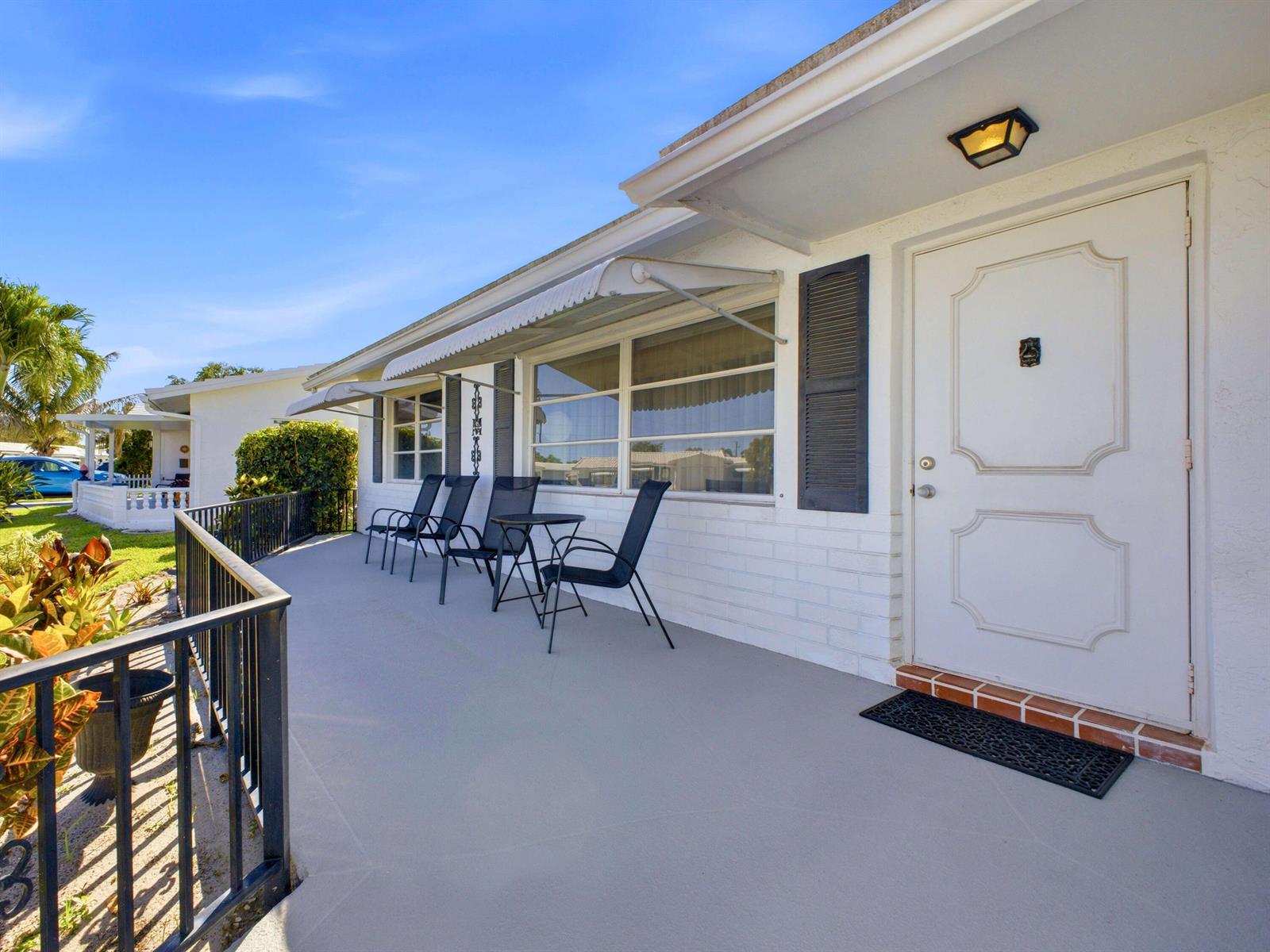 A white house exterior features a gray patio with black chairs and a metal railing — 2020 SW 17th Avenue, Boynton Beach FL 33426, BOYNTON BEACH, FL