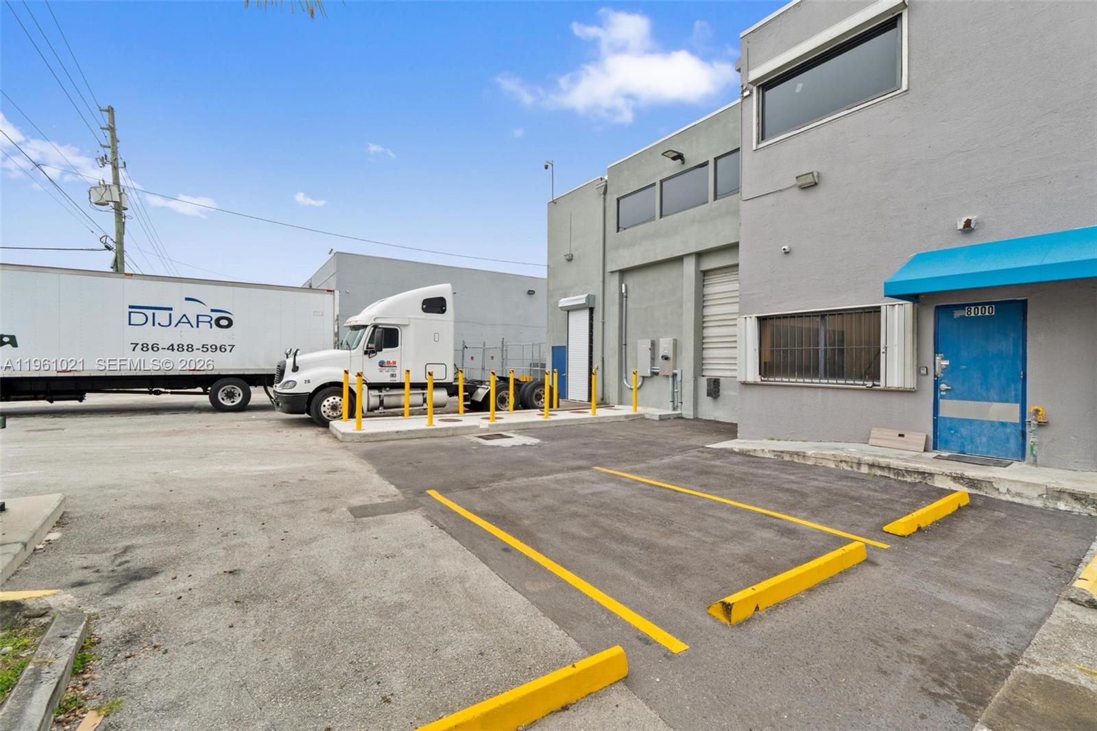 An exterior view of a commercial building with a blue door and a parked semi-truck — 8000 NW 68th St, Medley FL 33166, MEDLEY, FL