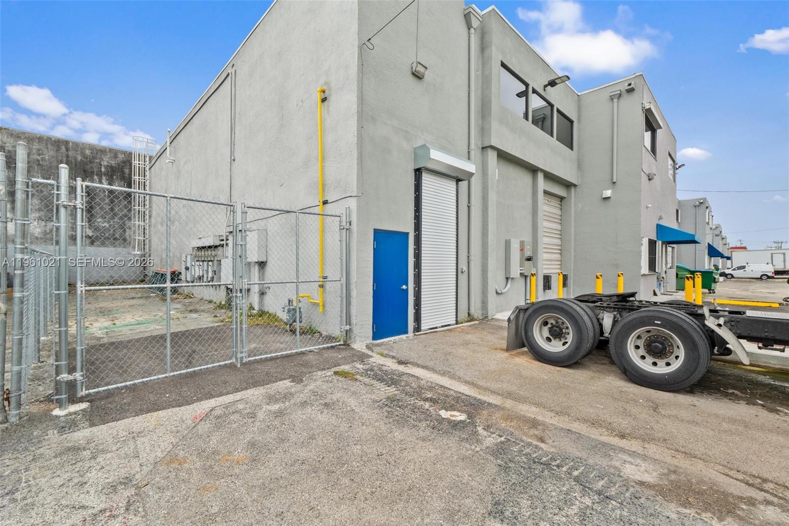 The exterior of a gray industrial warehouse building features a loading dock and chain-link fence — 8000 NW 68th St, Medley FL 33166, MEDLEY, FL