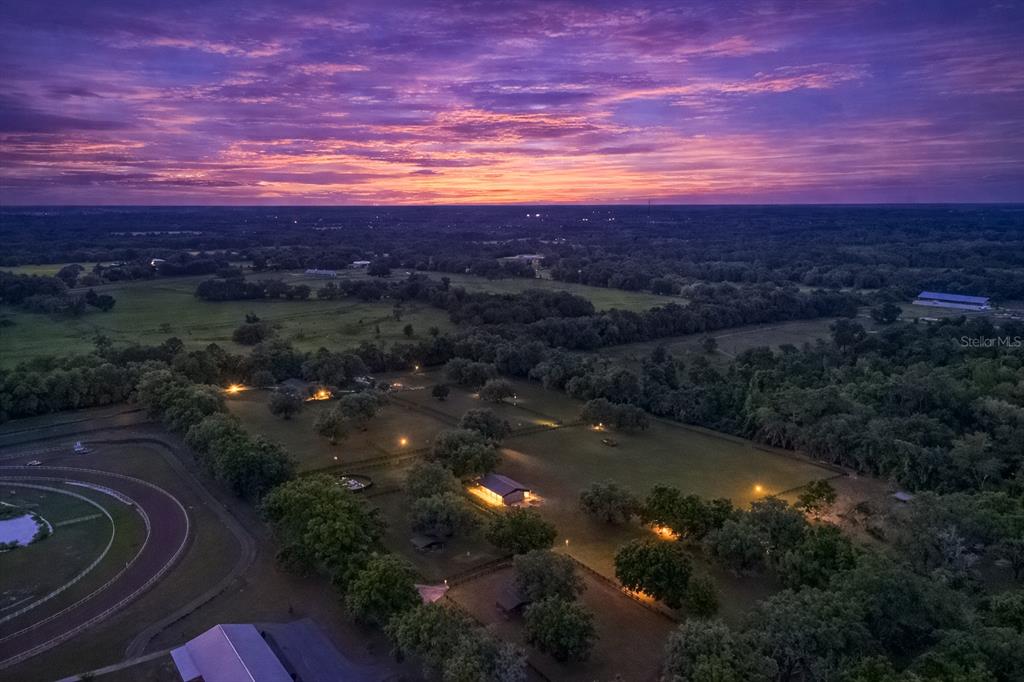 An aerial view of a rural property featuring a horse track and illuminated barns at sunset — 14650 NW 160TH AVENUE, WILLISTON, FL
