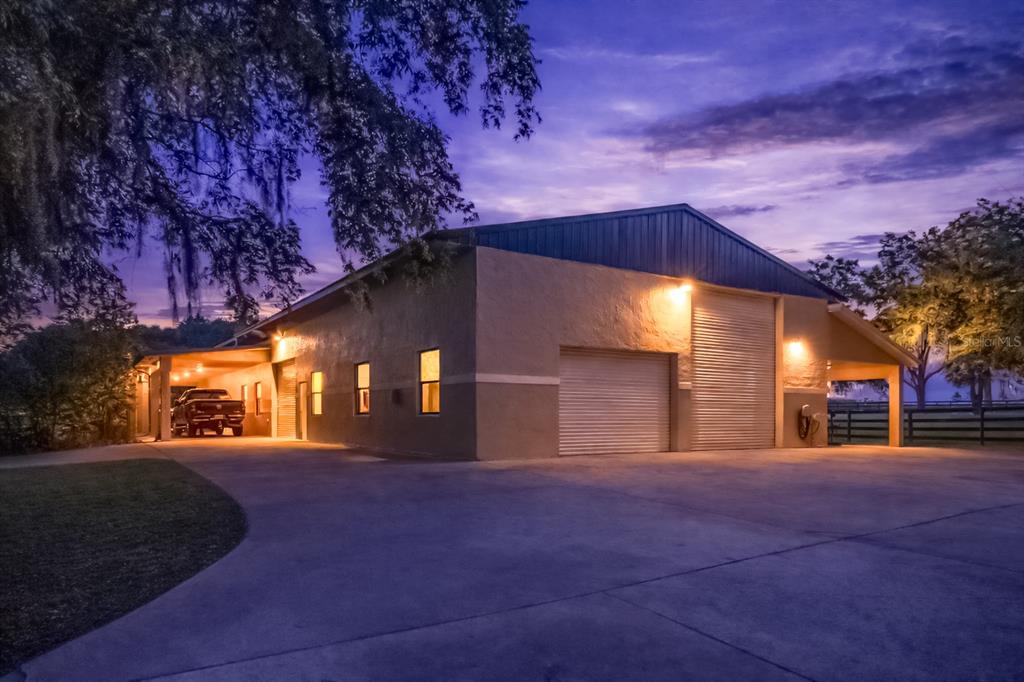 A large, tan metal-sided workshop building with two garage doors and a covered parking area — 14650 NW 160TH AVENUE, WILLISTON, FL