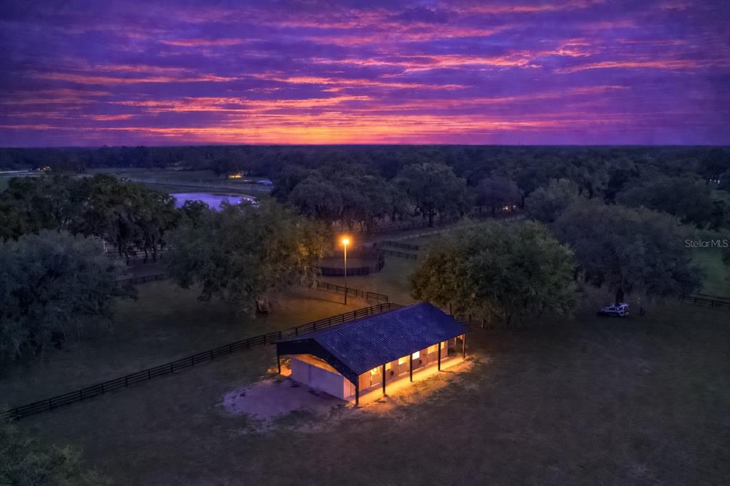 An aerial view of a small horse stable illuminated at night under a vibrant sunset — 14650 NW 160TH AVENUE, WILLISTON, FL