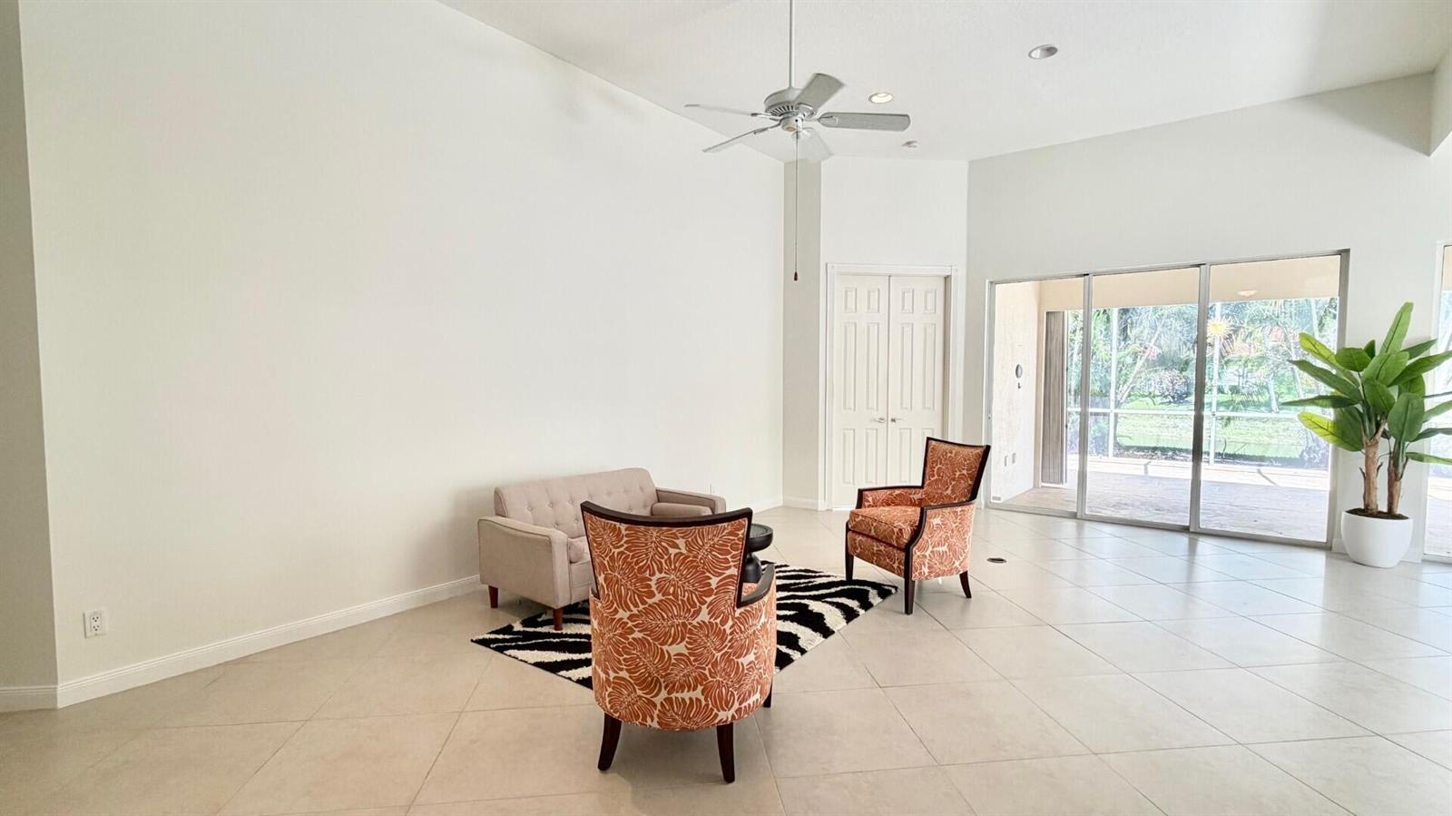 A living room features white walls, tile flooring, a ceiling fan, and sliding glass doors — 2704 Irma Lake Drive, West Palm Beach FL 33411, WEST PALM BEACH, FL