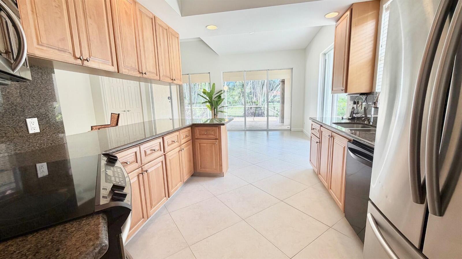 A kitchen with light wood cabinets, black granite countertops, and tile flooring leads to a patio — 2704 Irma Lake Drive, West Palm Beach FL 33411, WEST PALM BEACH, FL