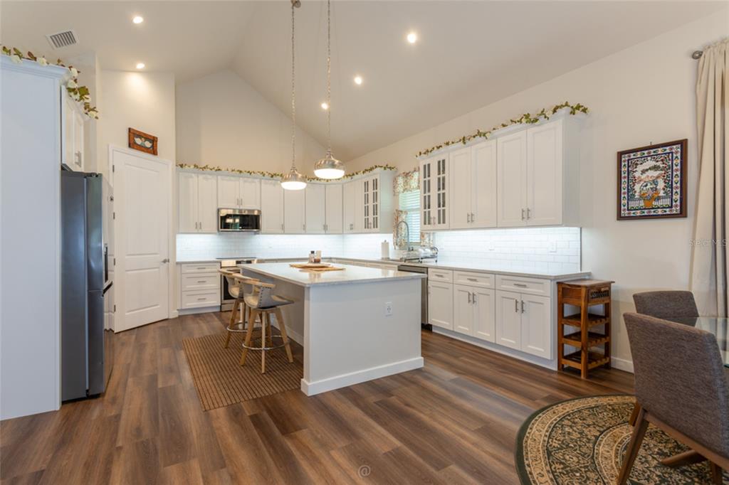 A kitchen features white cabinetry, a central island with bar seating, and wood-look flooring — 222 COUNTY ROAD 15, BUNNELL, FL