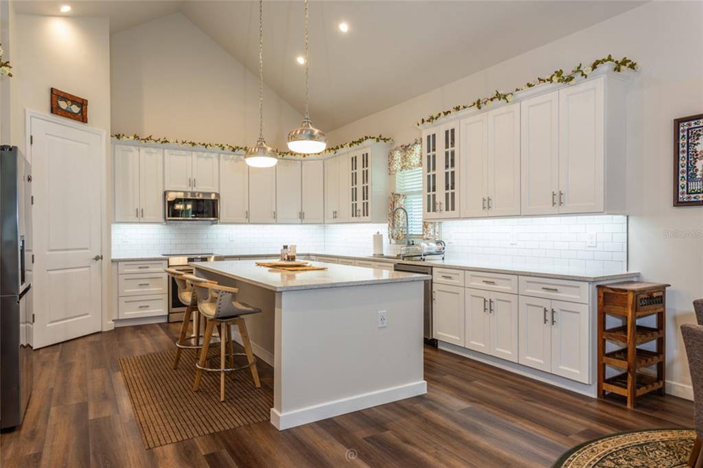 A bright kitchen features white cabinets, a central island with bar stools, and wood flooring — 222 COUNTY ROAD 15, BUNNELL, FL