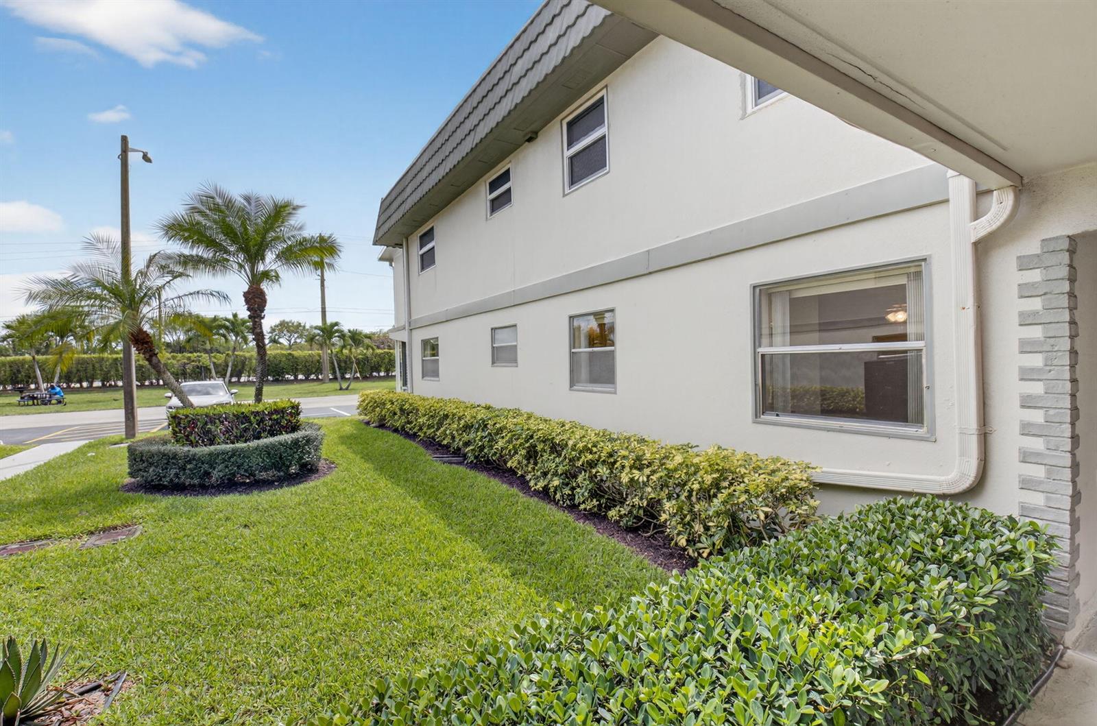 The exterior of a two-story building features white stucco walls, a shingled roof, and landscaping — 204 Flanders E, Delray Beach FL 33484, DELRAY BEACH, FL