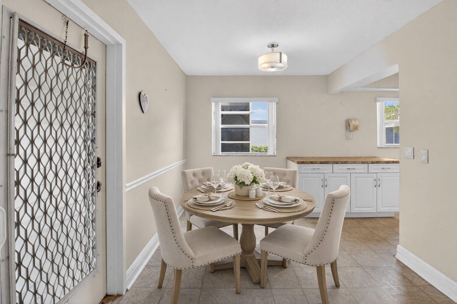A dining area features a round wooden table with four upholstered chairs and tile flooring — 204 Flanders E, Delray Beach FL 33484, DELRAY BEACH, FL