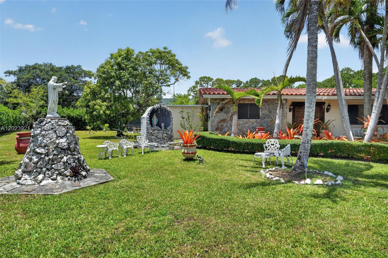 A front yard features a stone statue, a religious grotto, and a single-story house — 8461 SW 68th St Rd, Miami FL 33143, MIAMI, FL