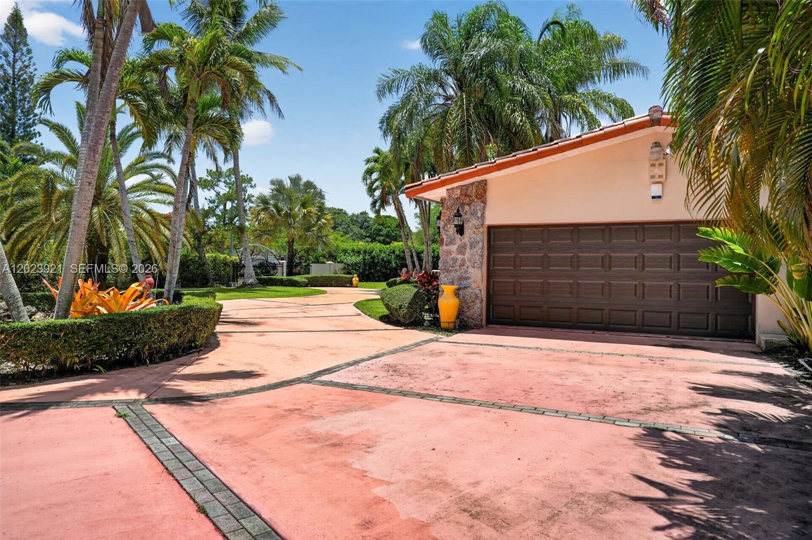 A paved driveway leads to a garage with stone accents surrounded by tropical palm trees — 8461 SW 68th St Rd, Miami FL 33143, MIAMI, FL