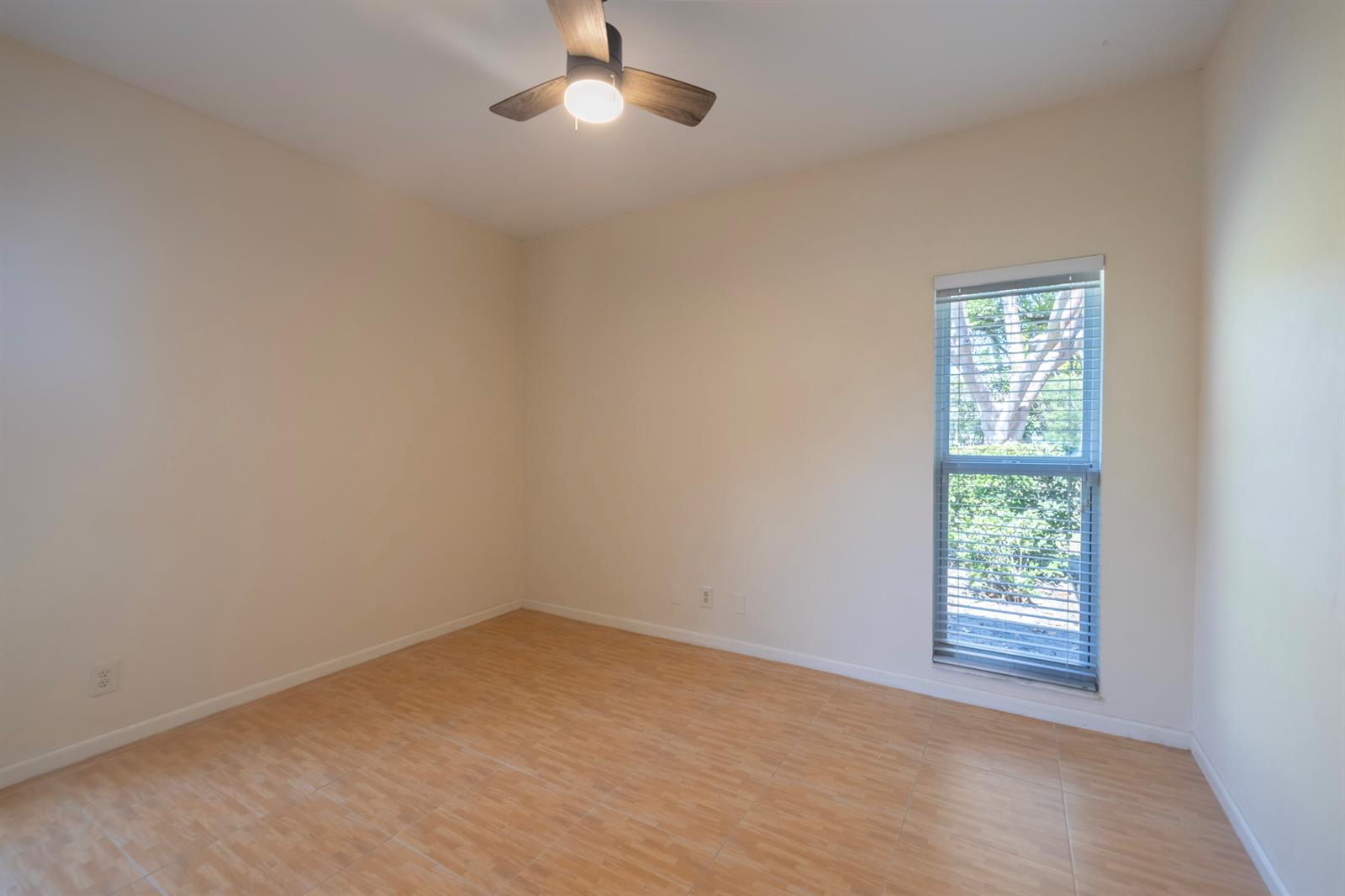 An empty bedroom features light-colored walls, wood-look tile flooring, a ceiling fan, and one window — 10195 Greentrail Drive, Boynton Beach FL 33436, BOYNTON BEACH, FL