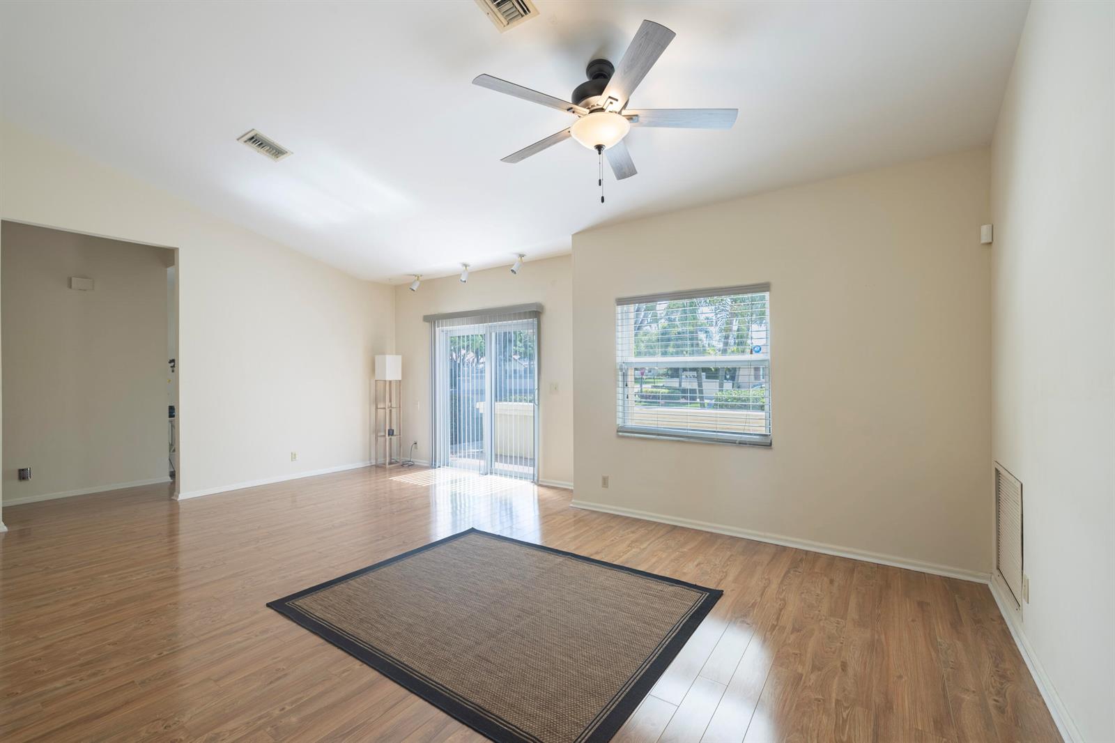 An empty living room features light wood-look flooring, a ceiling fan, and a sliding glass door — 10195 Greentrail Drive, Boynton Beach FL 33436, BOYNTON BEACH, FL