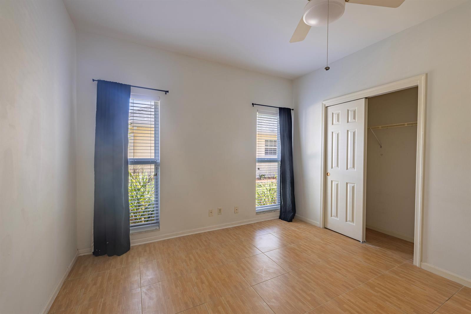 An empty bedroom features light-colored tile flooring, two windows with dark curtains, and a closet — 10195 Greentrail Drive, Boynton Beach FL 33436, BOYNTON BEACH, FL