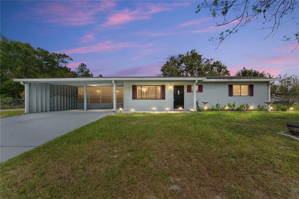 A single-story house with a carport, gray siding, and a front lawn at dusk — 9981 SW 103RD PLACE, OCALA, FL