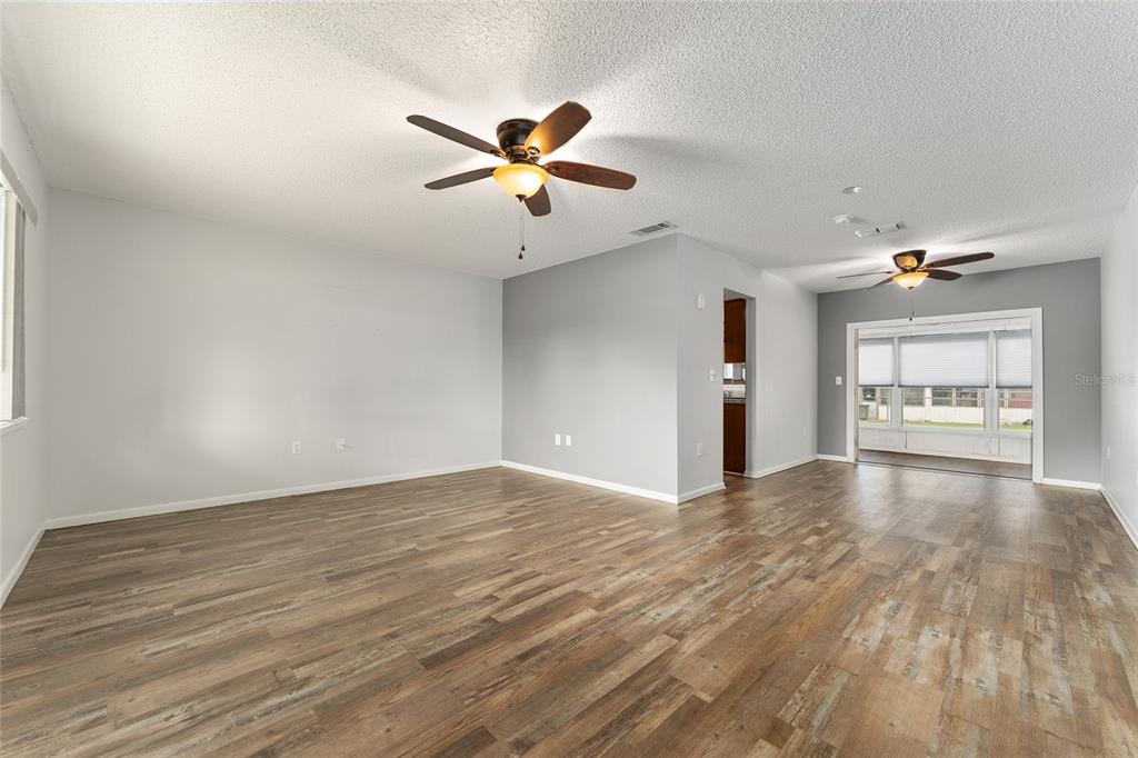 An empty living room features light gray walls, wood-look flooring, and two ceiling fans — 9981 SW 103RD PLACE, OCALA, FL