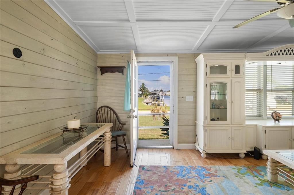 A sunroom with wood-paneled walls, a glass-topped table, and a door opening to a canal — 4220 DELTONA DRIVE, PUNTA GORDA, FL