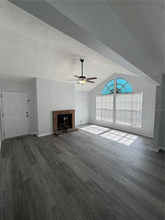 A living room features gray wood-look flooring, a brick fireplace, and a vaulted ceiling — 645 STAFFORD TERRACE UNIT 156, ALTAMONTE SPRINGS, FL