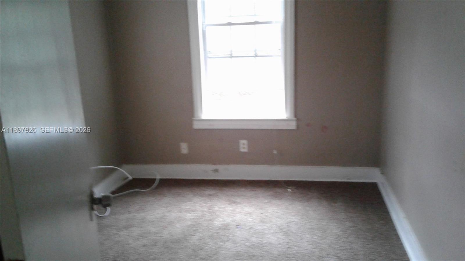 An empty room features beige walls, a single window, and brown carpeting — 2748 Broadway # 0, Jacksonville FL 32254, JACKSONVILLE, FL
