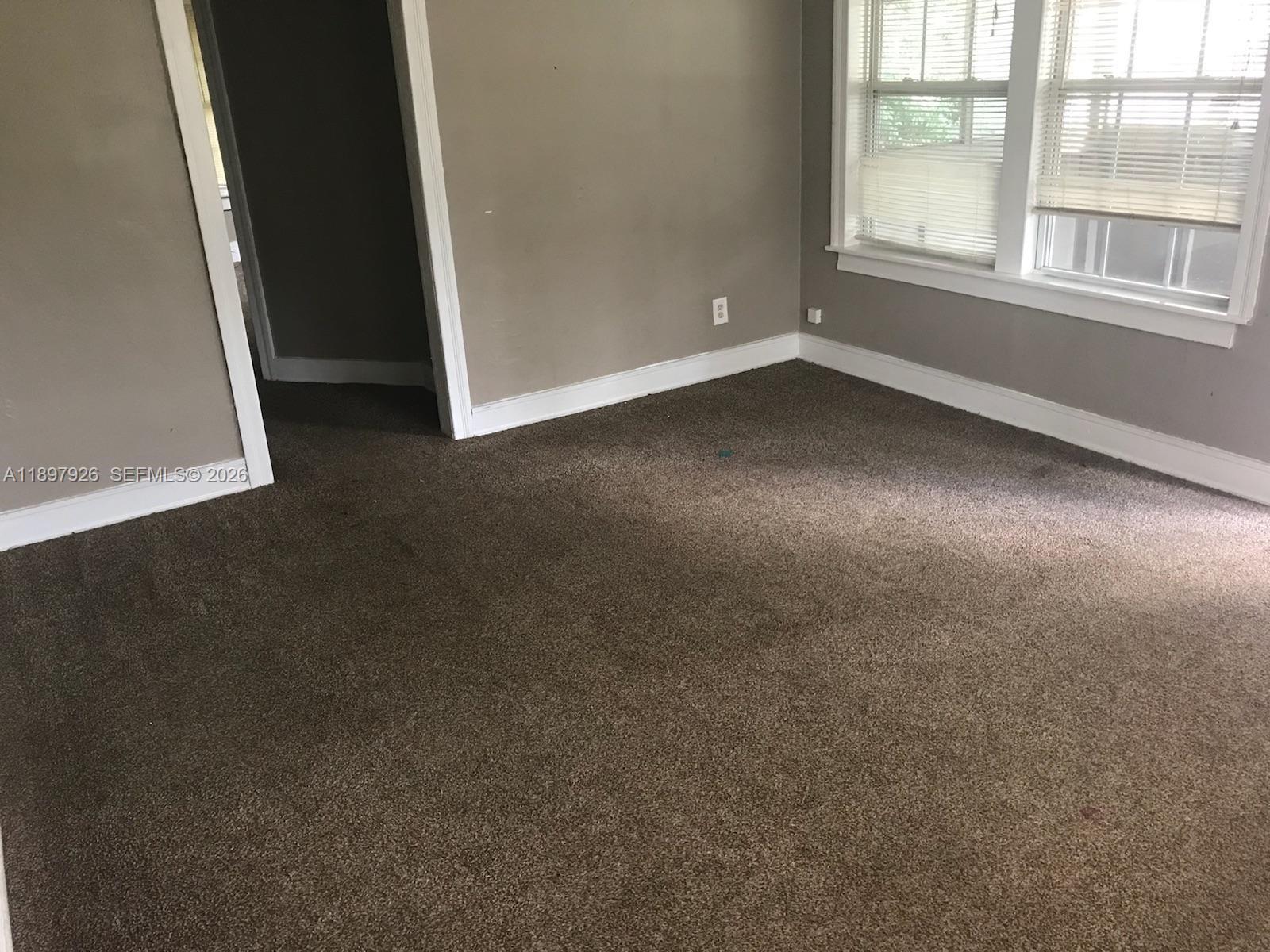 An empty room features brown carpeting, gray walls, white trim, and two windows with blinds — 2748 Broadway # 0, Jacksonville FL 32254, JACKSONVILLE, FL