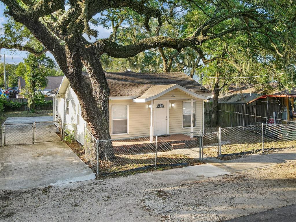 A single-story house with light siding and a large oak tree in the front yard — 2116 E ELLICOTT STREET, TAMPA, FL