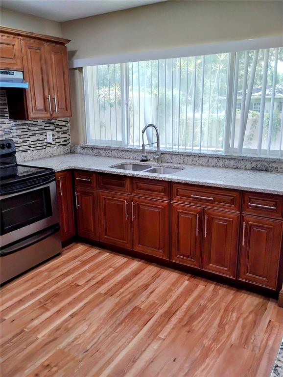 A kitchen features wood cabinets, granite countertops, a stainless steel stove, and light wood flooring — 11721 RAINTREE DRIVE, TAMPA, FL