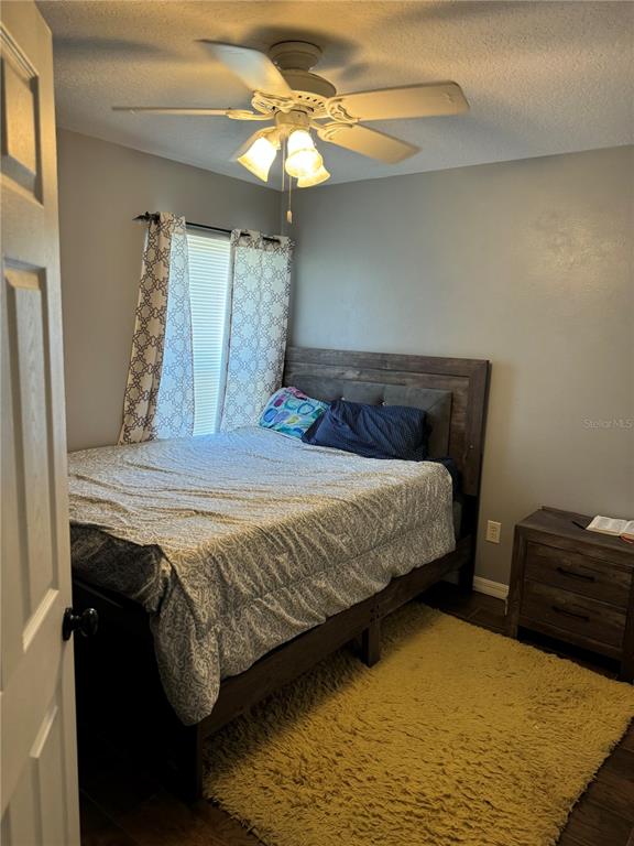 A bedroom features a wooden bed frame, a yellow rug, and a ceiling fan — 5427 BRYCE CANYON DRIVE, KISSIMMEE, FL