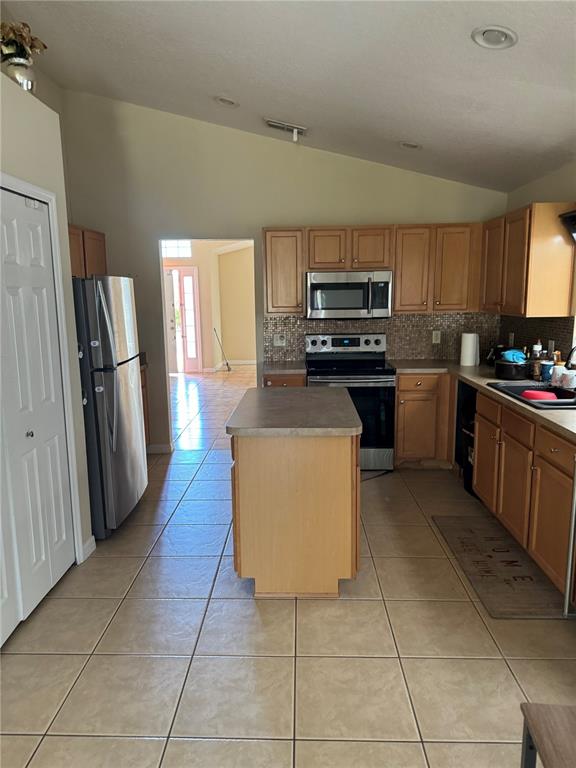 A kitchen features light wood cabinets, stainless steel appliances, a central island, and tile flooring — 5427 BRYCE CANYON DRIVE, KISSIMMEE, FL