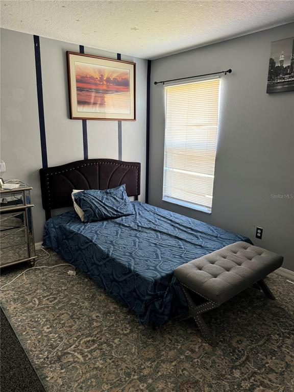 A bedroom features a dark upholstered headboard, a blue patterned bedspread, and a gray bench — 5427 BRYCE CANYON DRIVE, KISSIMMEE, FL