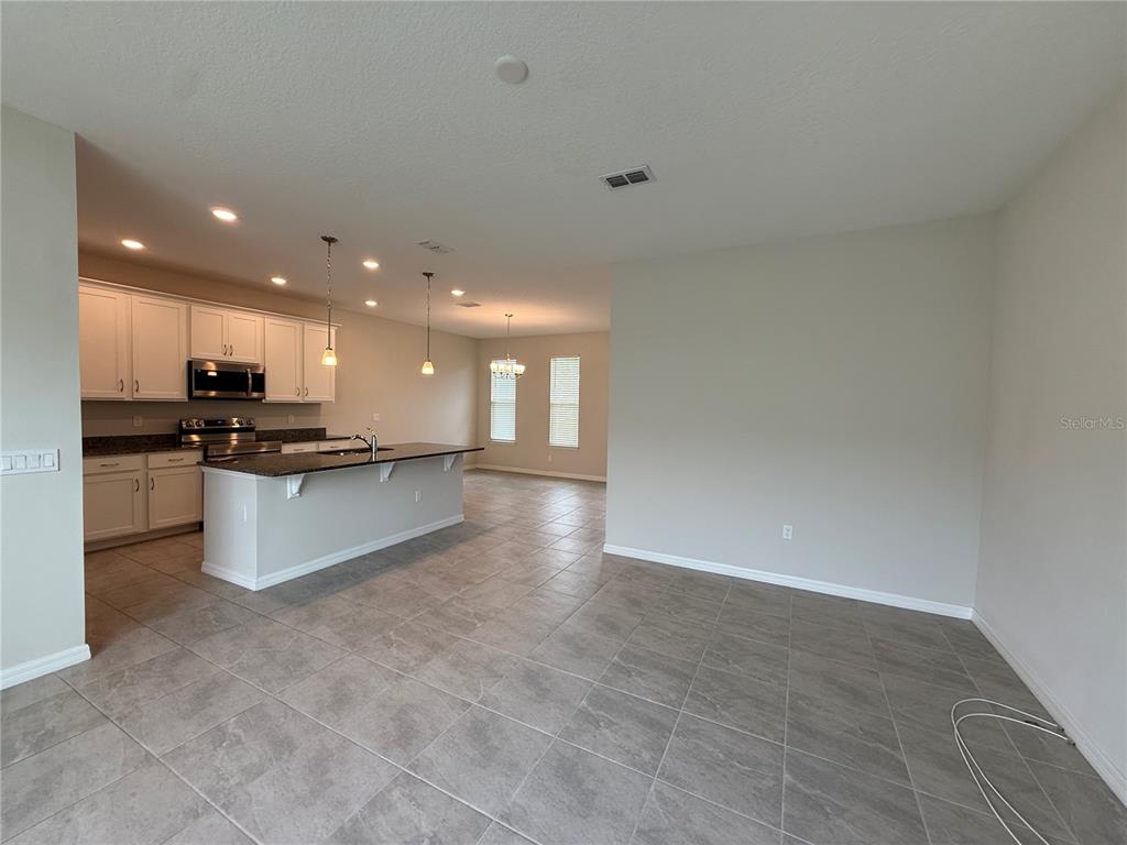 An open-concept kitchen features white cabinets, granite countertops, a center island, and tile flooring — 5072 AVALON PARK BOULEVARD, WESLEY CHAPEL, FL