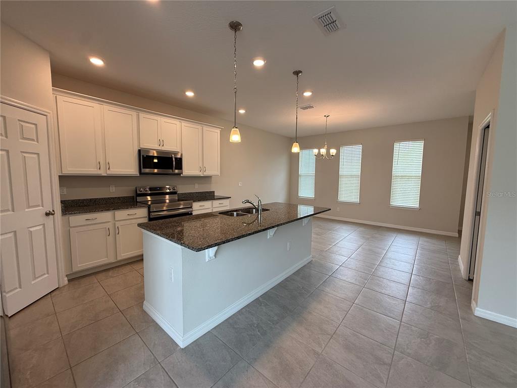 A kitchen features white cabinets, granite countertops, a central island, and tile flooring — 5072 AVALON PARK BOULEVARD, WESLEY CHAPEL, FL