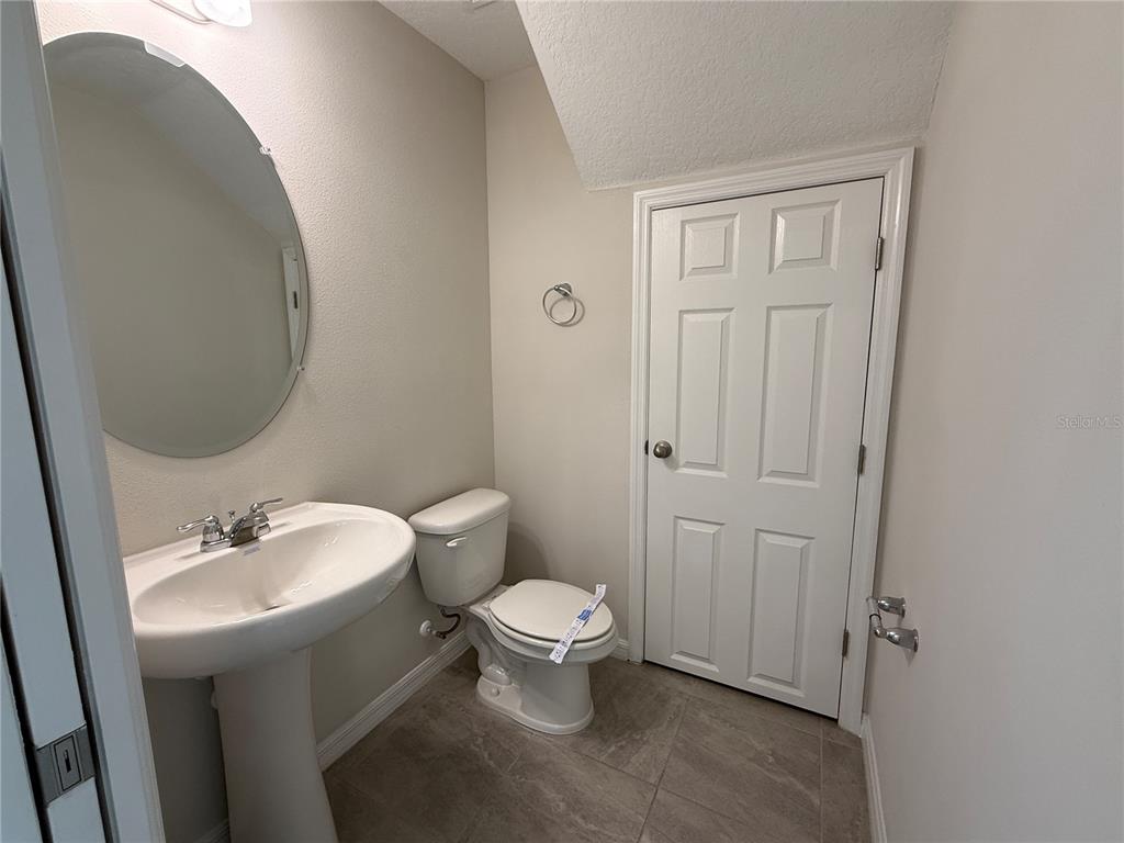 A half bathroom features a pedestal sink, an oval mirror, and a white toilet — 5072 AVALON PARK BOULEVARD, WESLEY CHAPEL, FL