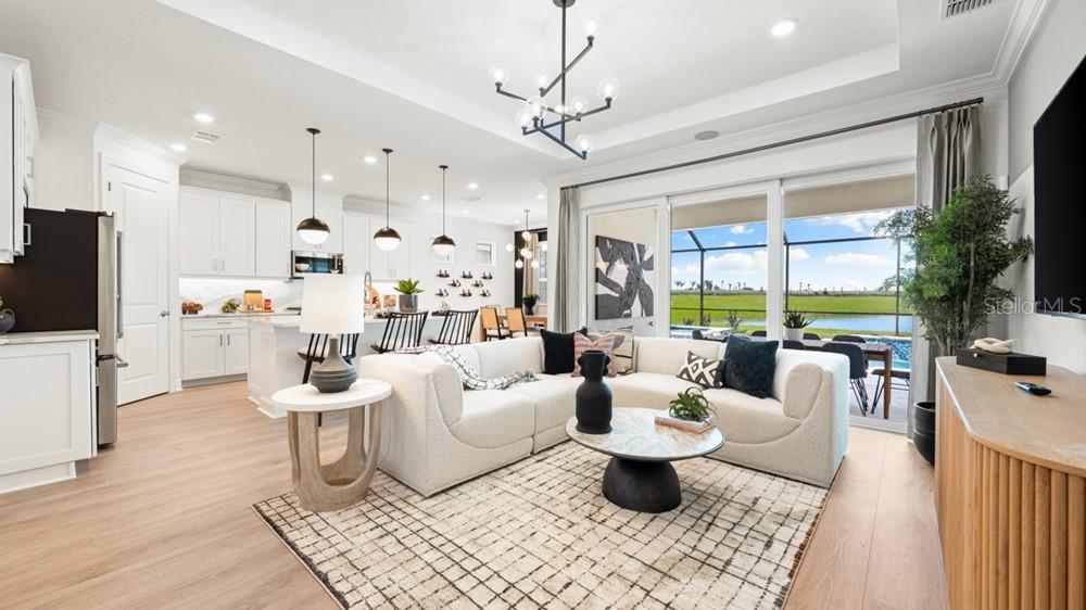 An open-concept living room and kitchen feature white cabinetry, a sectional sofa, and pool views — 10610 ECLIPSE STREET, SARASOTA, FL
