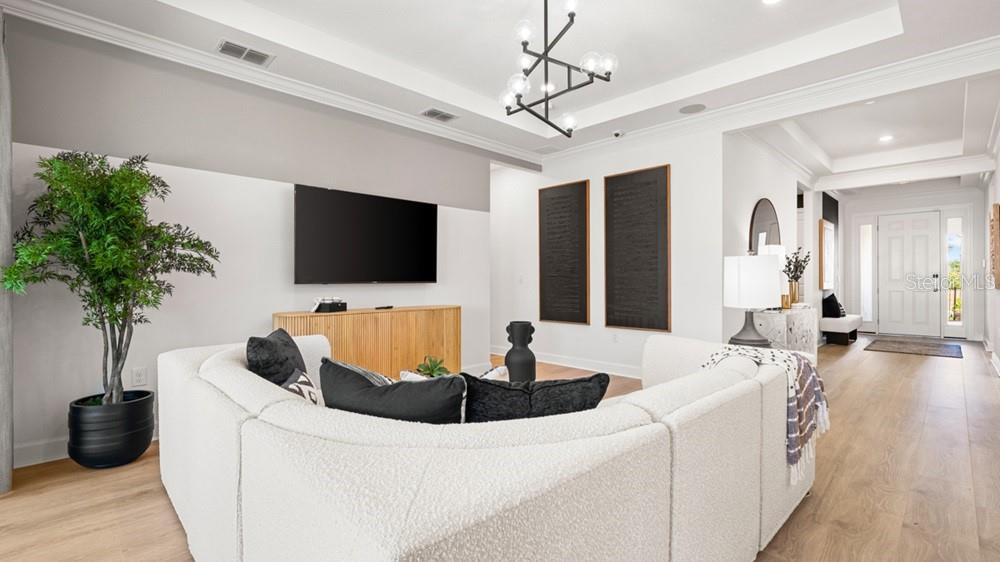 A living room features a white curved sofa, a wall-mounted television, and a modern chandelier — 10610 ECLIPSE STREET, SARASOTA, FL