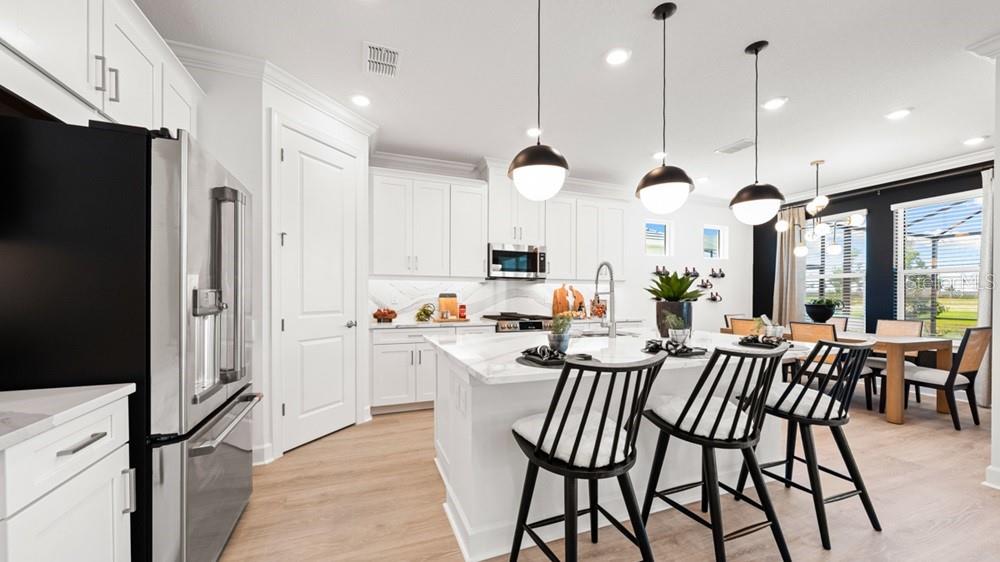 A modern white kitchen features a marble-topped island with black stools and stainless steel appliances — 10610 ECLIPSE STREET, SARASOTA, FL