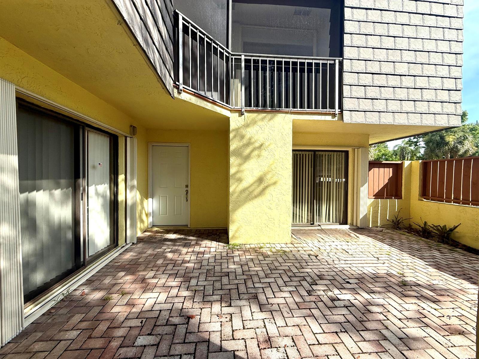 A paved patio area sits beneath a second-story balcony with a yellow stucco exterior — 3100 SE Brook Street, Stuart FL 34997, STUART, FL
