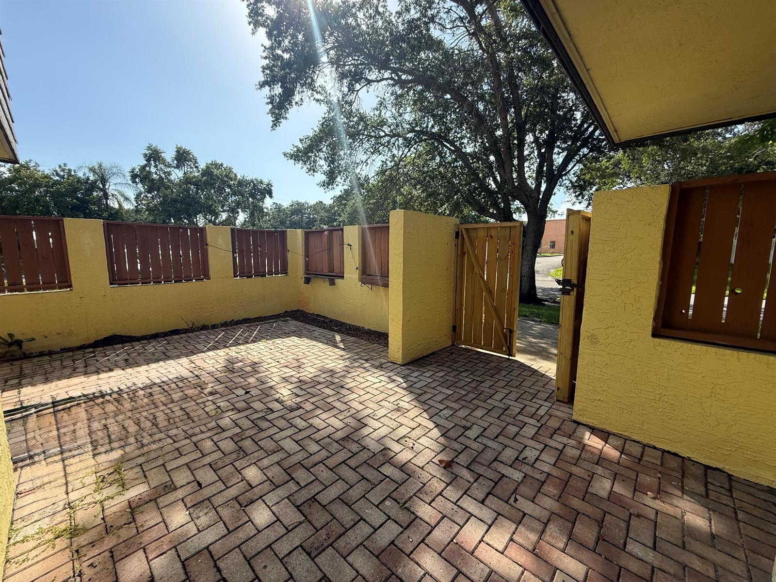 A brick-paved patio enclosed by yellow stucco walls with brown wooden fence inserts — 3100 SE Brook Street, Stuart FL 34997, STUART, FL
