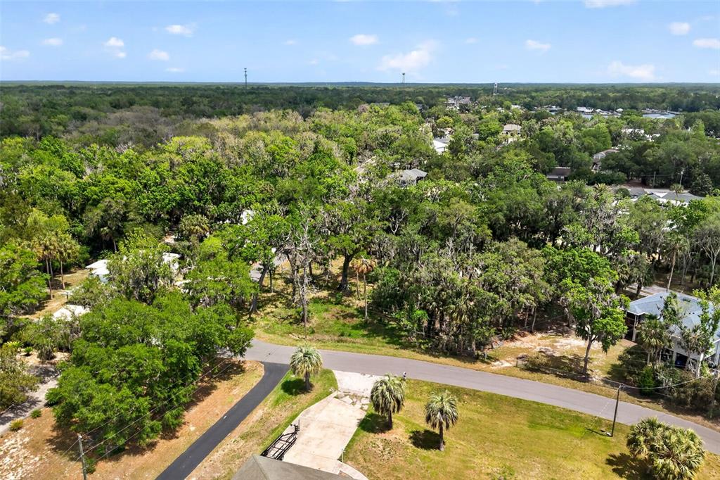 An aerial view shows a paved road winding through a wooded residential area with houses — 580 NW 14TH PLACE, CRYSTAL RIVER, FL