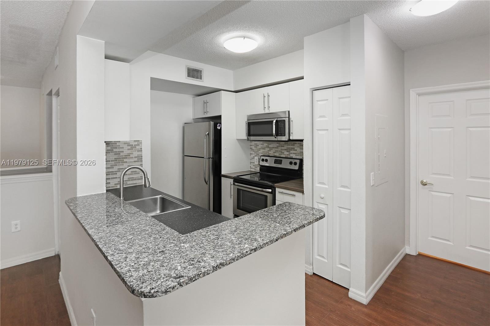 A kitchen features granite countertops, stainless steel appliances, white cabinets, and a breakfast bar — 2442 Centergate Dr # 202, Miramar FL 33025, MIRAMAR, FL