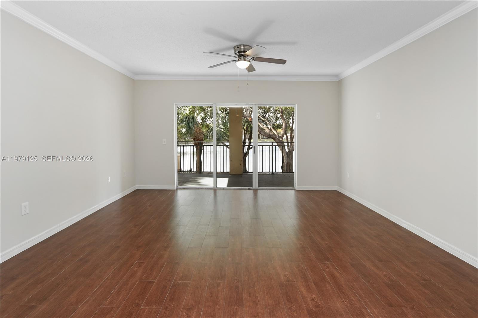 An empty room features wood-look flooring, a ceiling fan, and sliding glass doors to a balcony — 2442 Centergate Dr # 202, Miramar FL 33025, MIRAMAR, FL