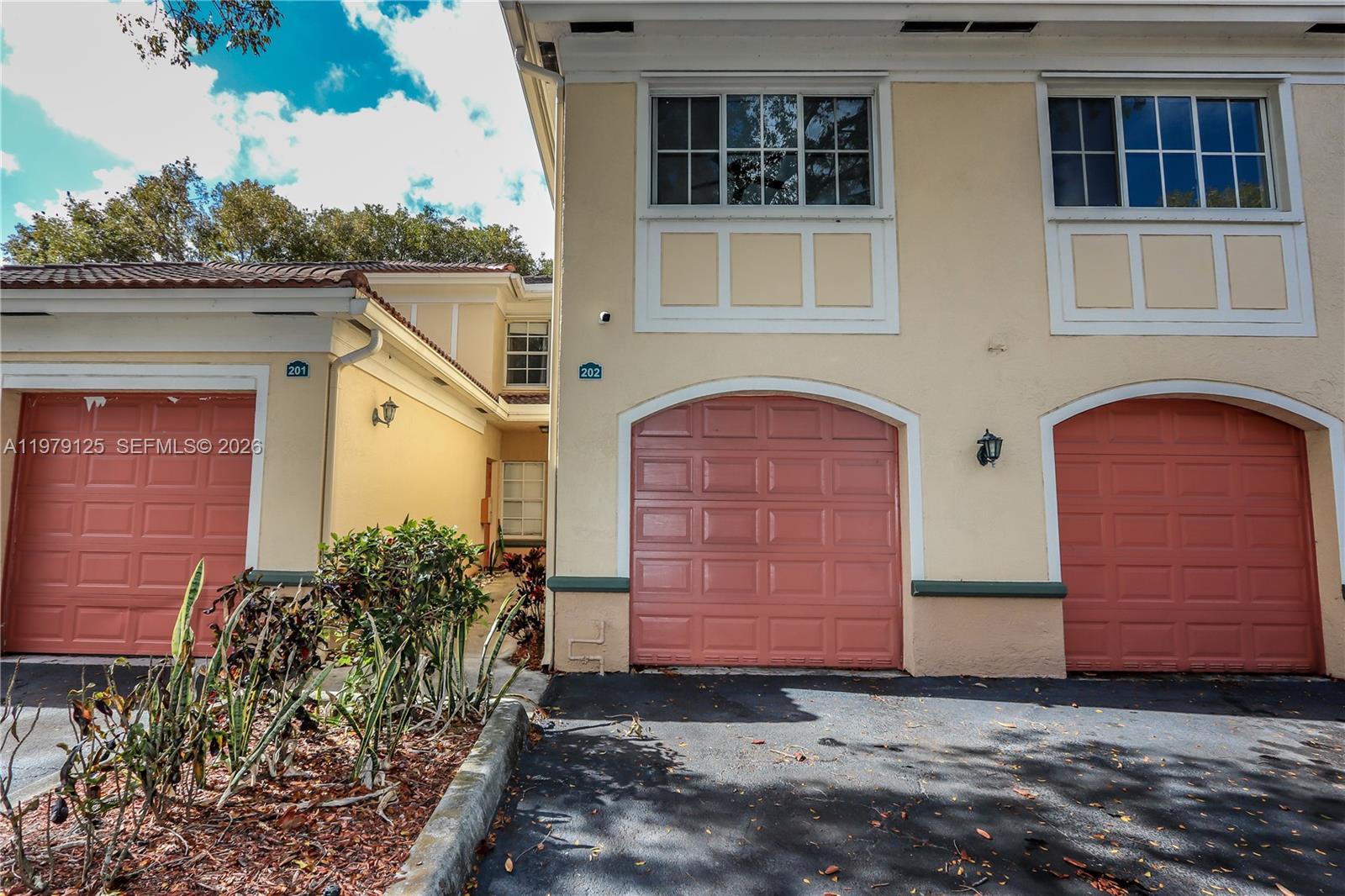 The exterior view shows three garage doors on a tan building with a small walkway — 2442 Centergate Dr # 202, Miramar FL 33025, MIRAMAR, FL