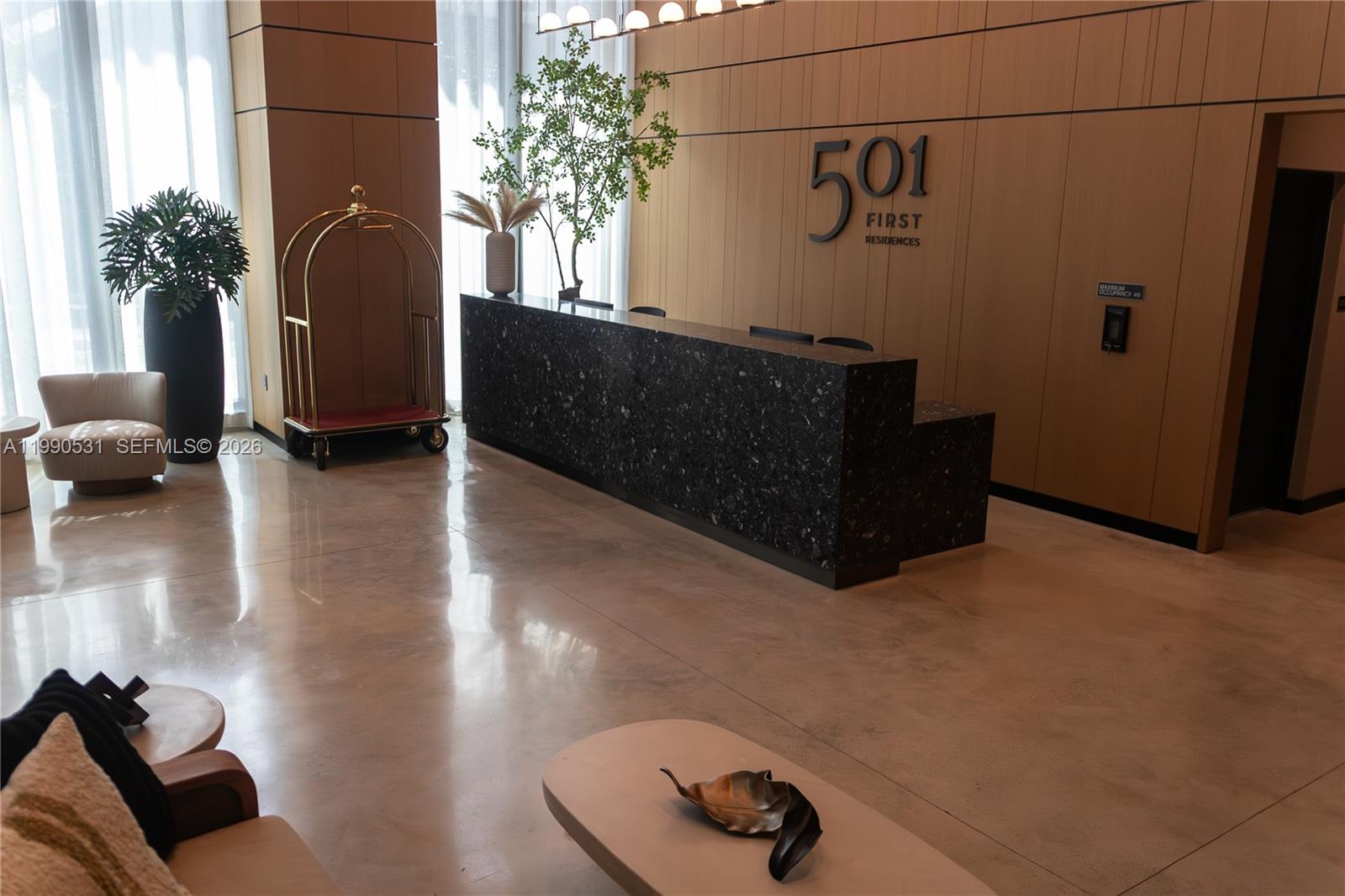 A modern lobby features a dark stone reception desk against a light wood paneled wall — 121 NE 5th St # 2611, Miami FL 33132, MIAMI, FL